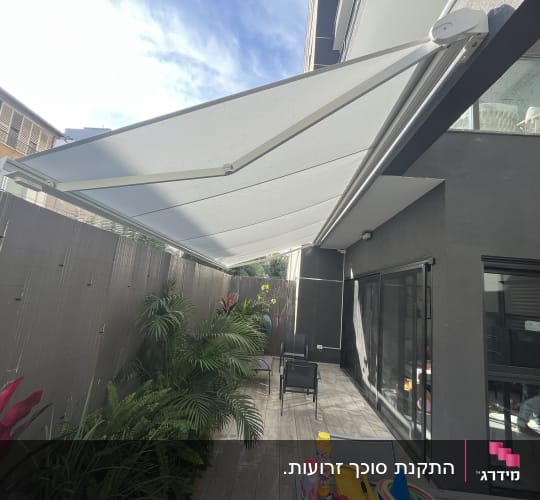 סוכך בד לבן נפתח מעל מרפסת חיצונית